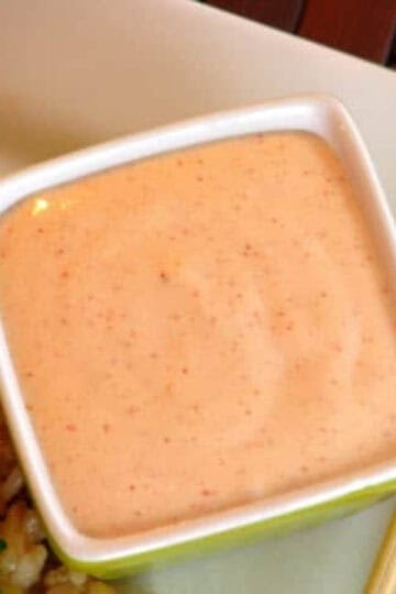Square bowl of yum yum sauce next to chop sticks on a plate.