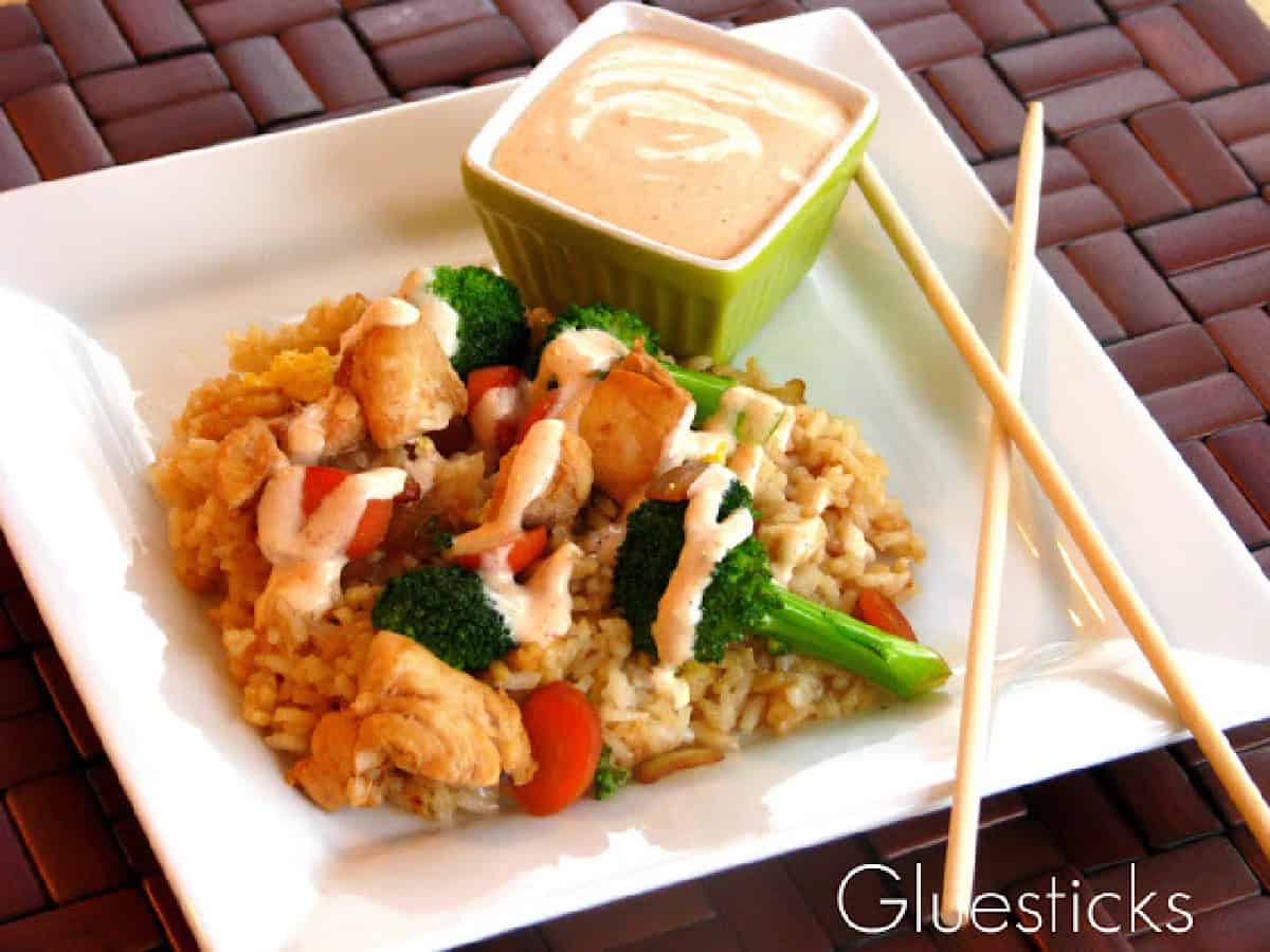 White plate of fried rice with small bowl of yum yum sauce and chopsticks.