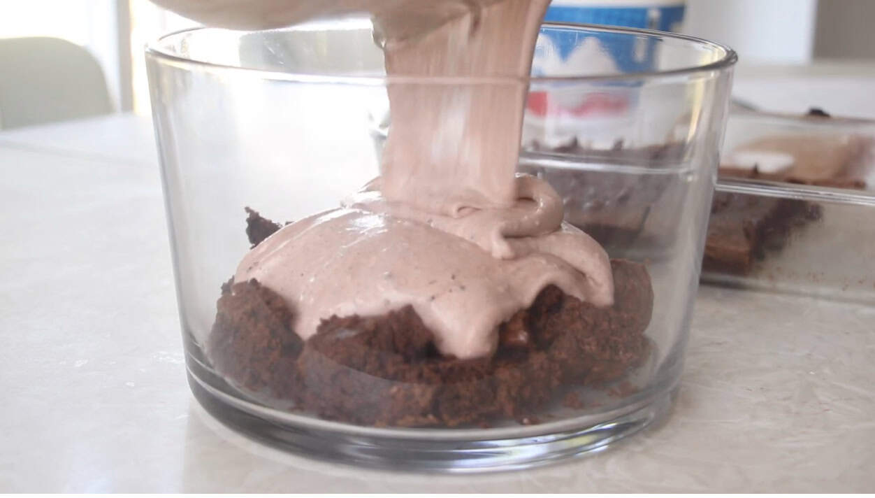 Glass trifle bowl with layer of brownies and pudding mixture poured on top.