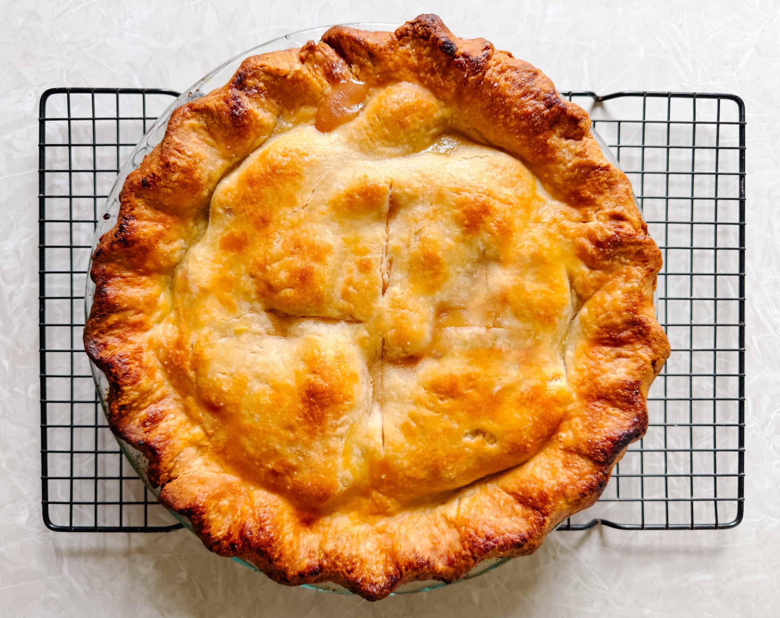 Peach pie on black wire rack.