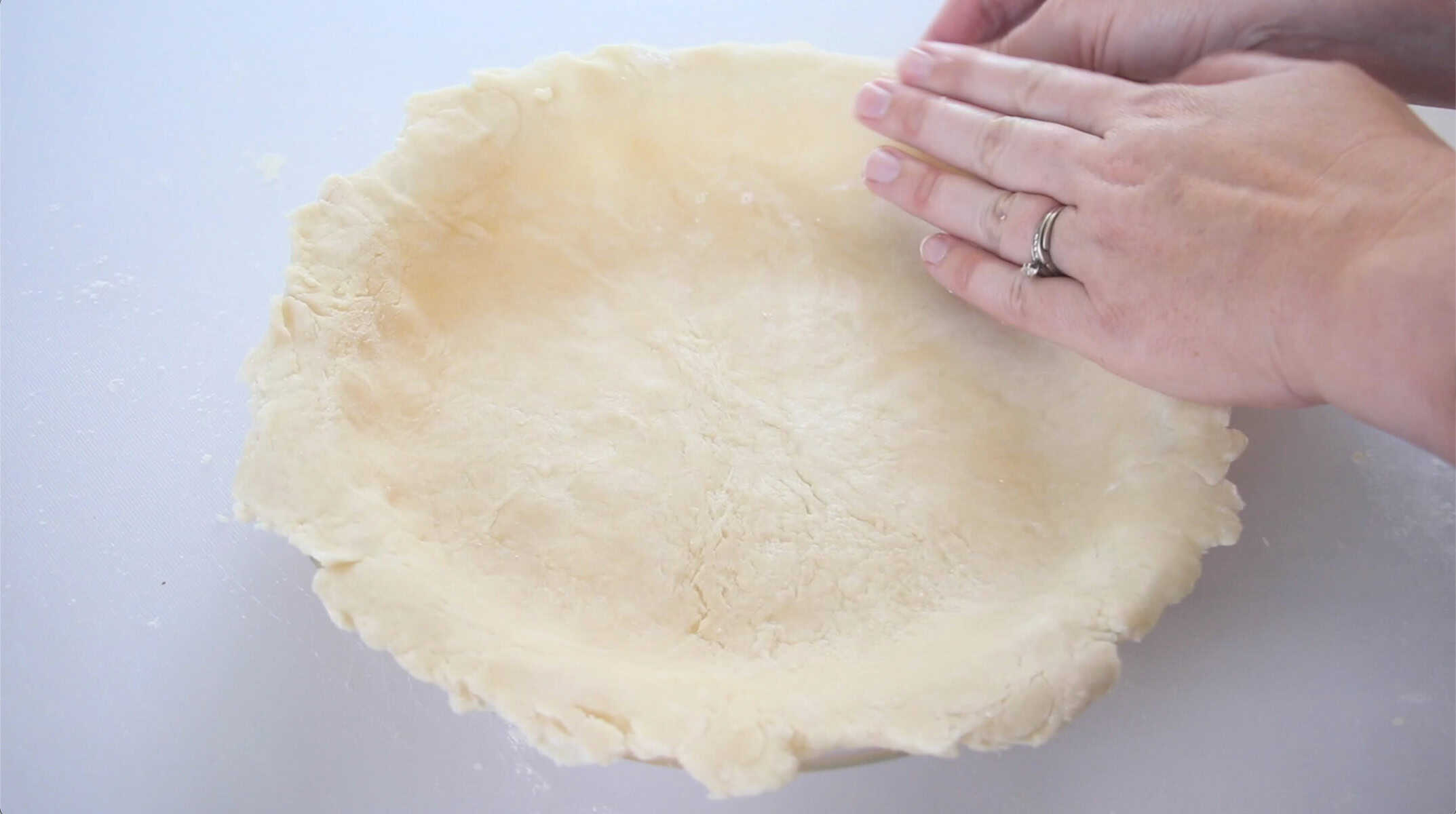 Hands pressing pie crust into pan pan.