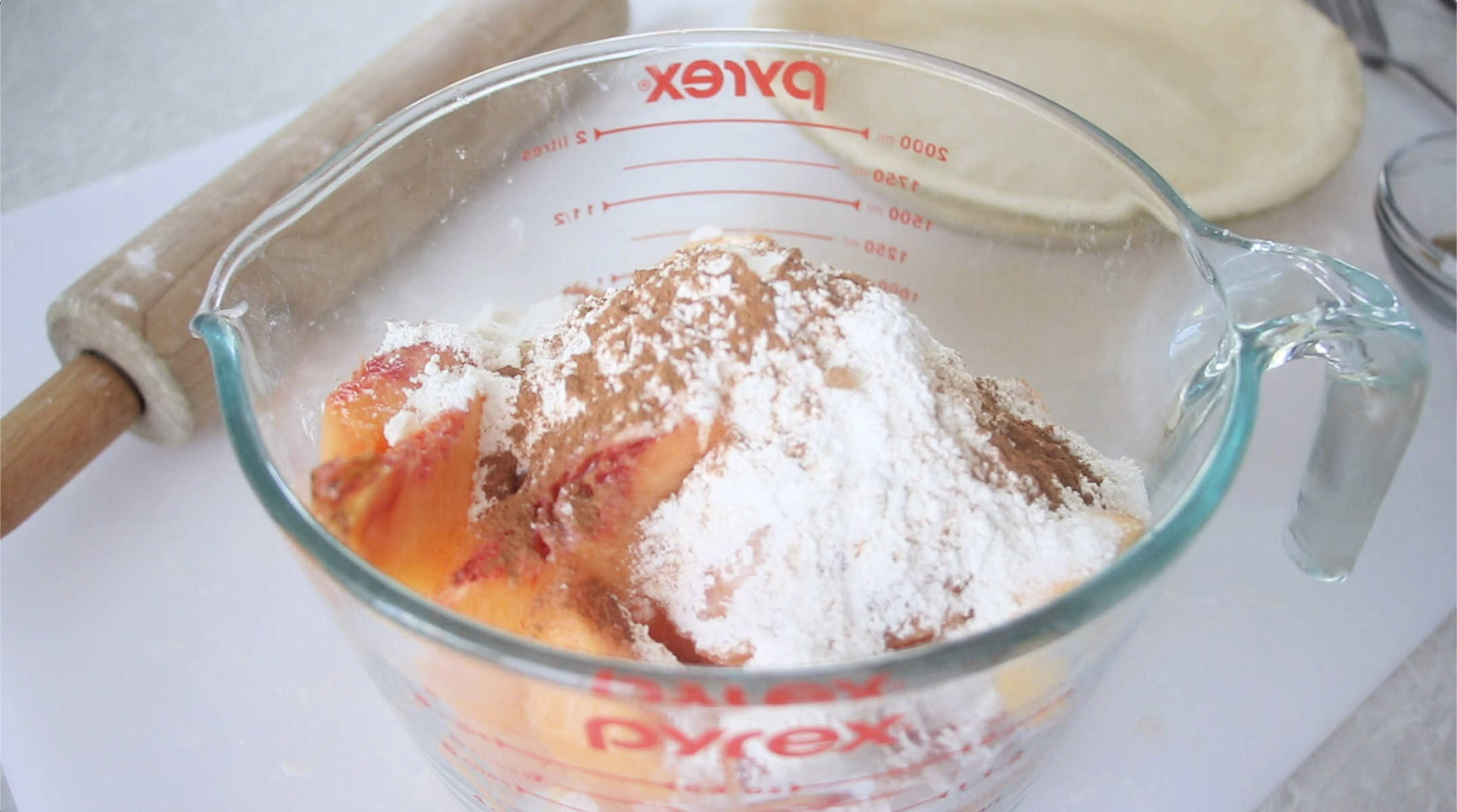 Glass bowl with chopped peaches, flour, cinnamon, salt, lemon juice and sugar.