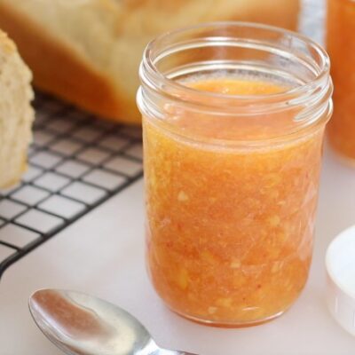 open jar of peach freezer jam next to a loaf of bread