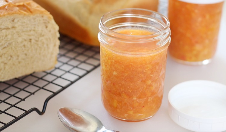 open jar of peach freezer jam next to a loaf of bread