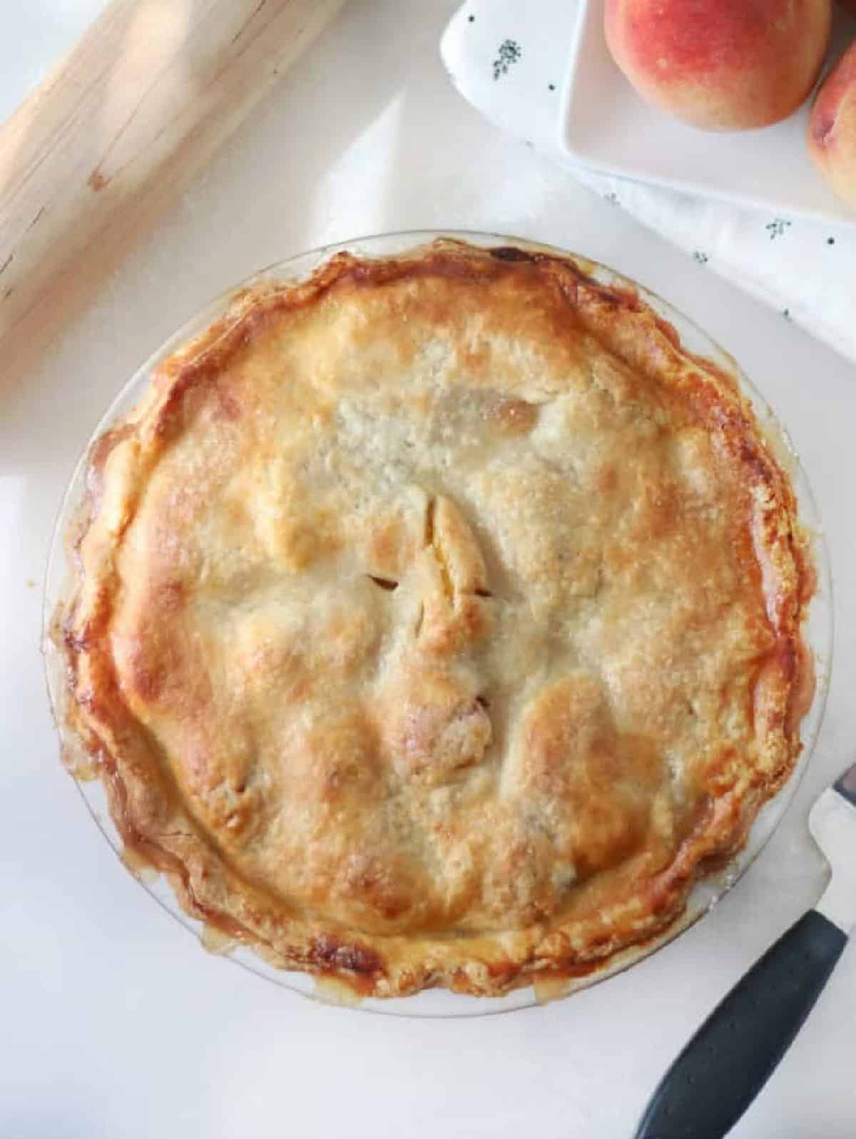Baked peach pie on cutting board with pie serving tool.