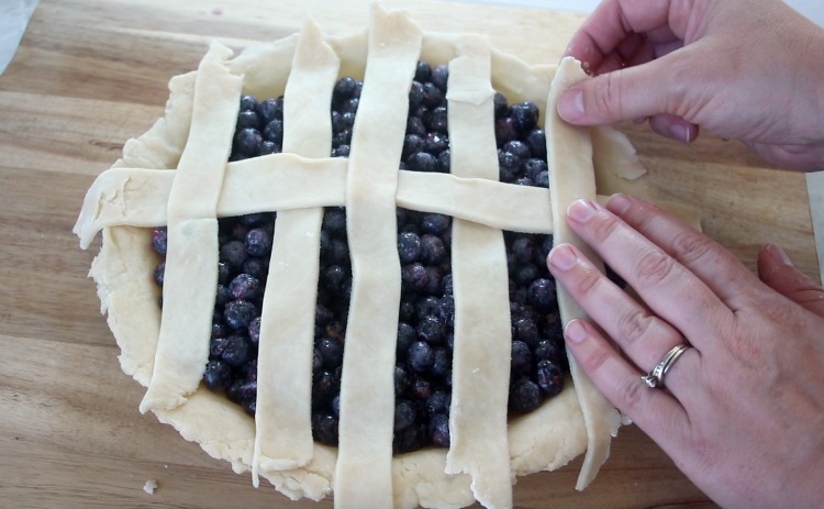 hands arranging pie crust strips for lattice top