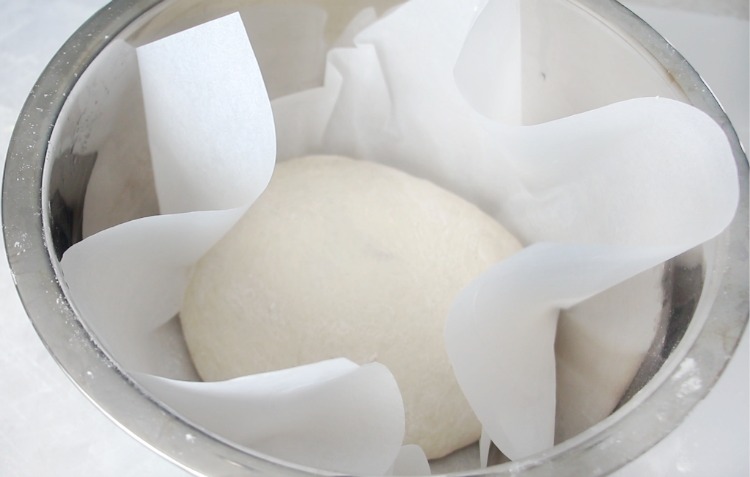 dough inside bowl with parchment paper for rising