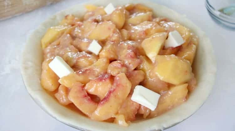 Pie pan with bottom crust and peach pie filling inside.