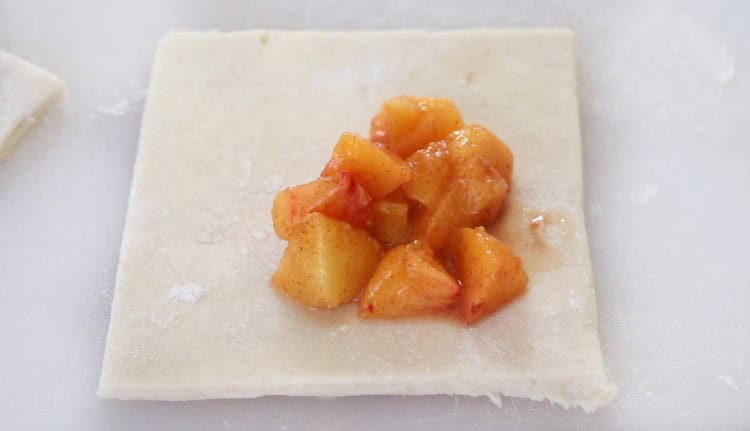 Spoonful of peach filling on puff pastry dough.