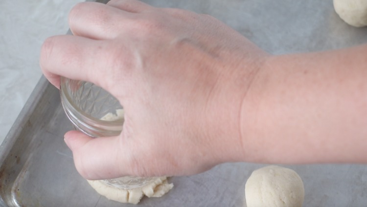 hand pressing glass onto ball of cookie dough to flatten