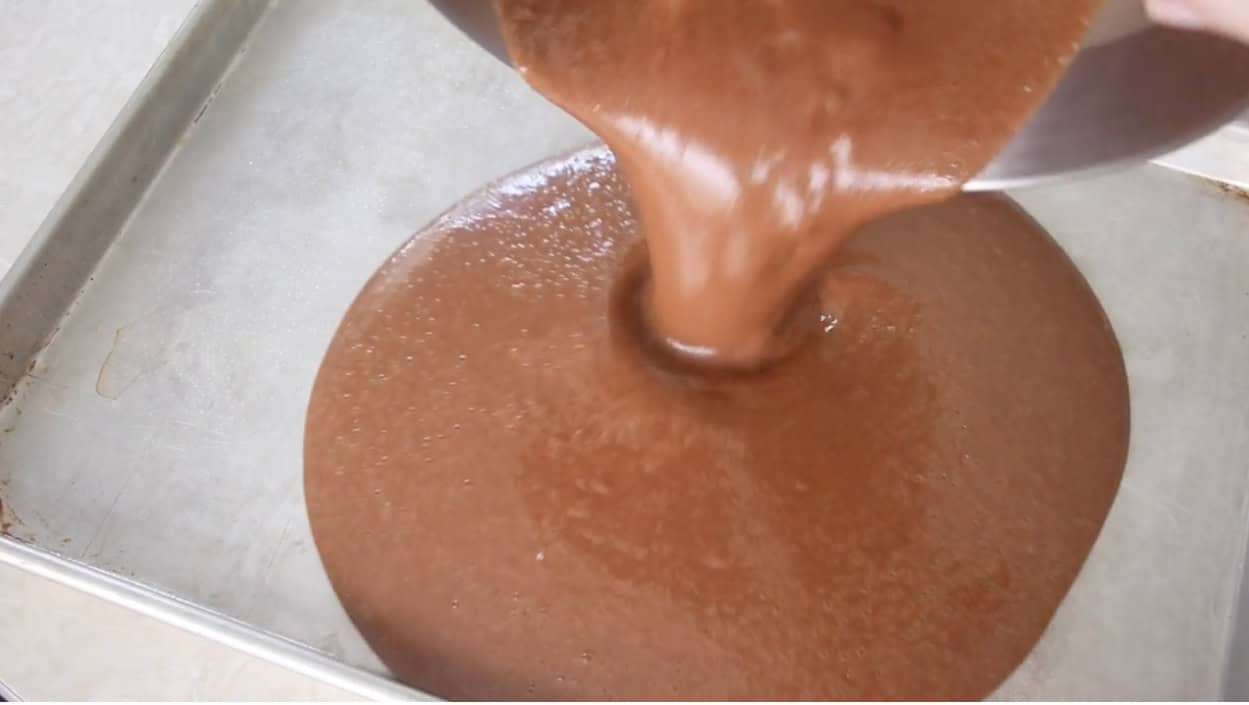 Chocolate cake batter being poured into sheet pan.