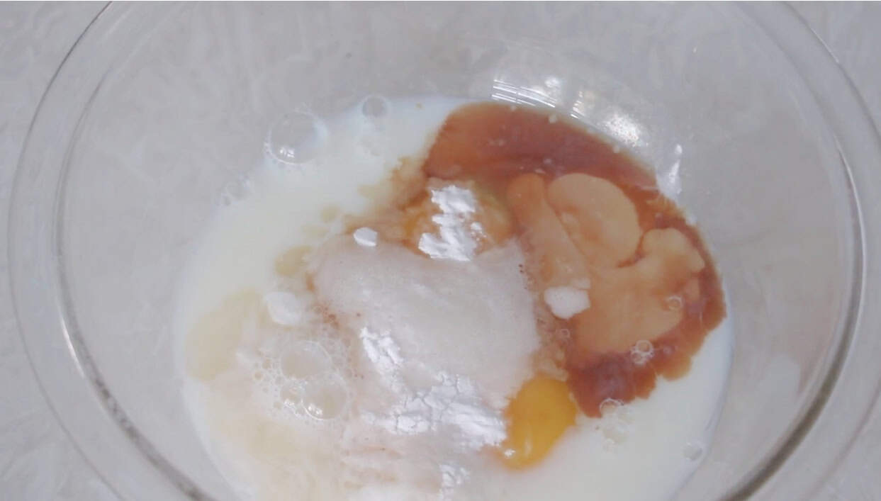 Glass mixing bowl with egg, milk, vanilla, vinegar and baking soda inside.