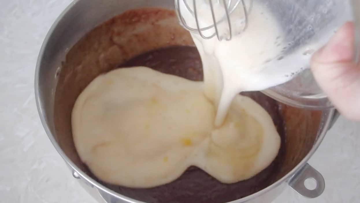 Egg and milk mixture being poured over chocolate cake batter in bowl.