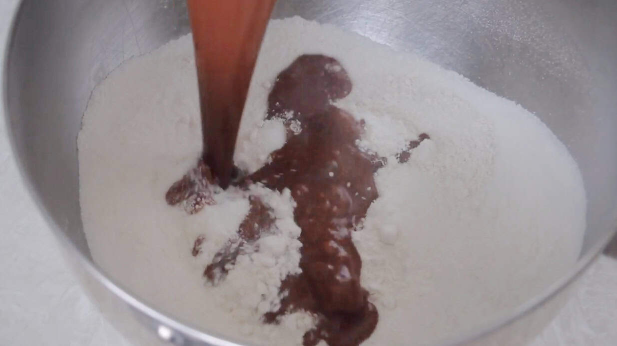 Chocolate and butter mixture poured over the flour mixture in a metal mixing bowl.