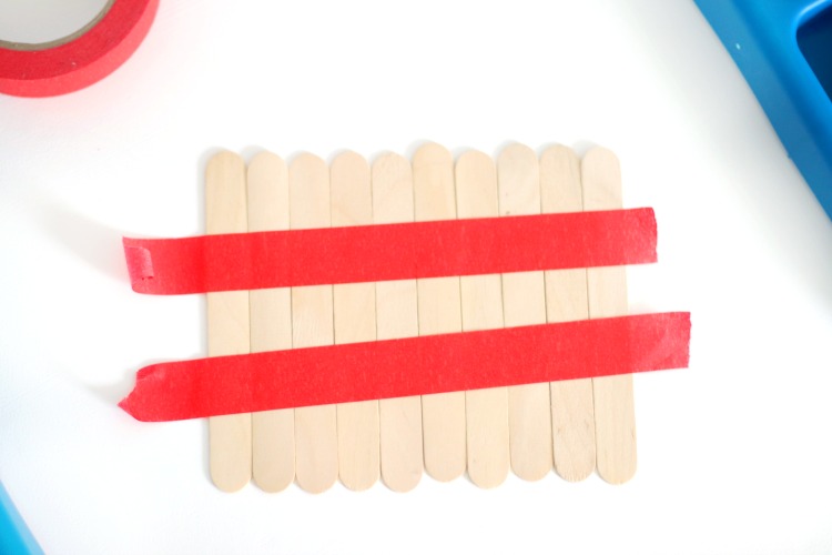 large popsicle sticks lined up on table with tape holding them in place