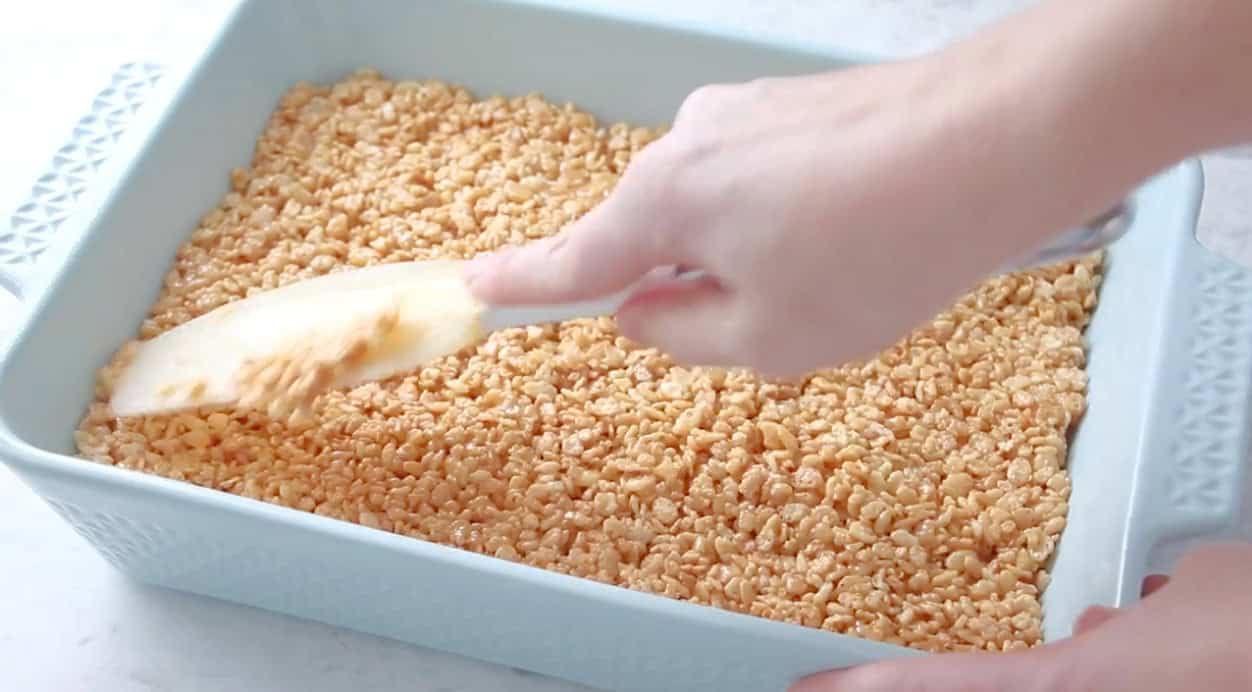 Rubber spatula pressed down against scotcheroos in pan. 