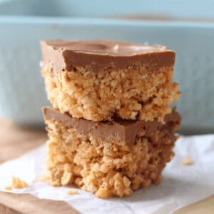Two scotcheroos cut into squares and stacked on parchment paper.