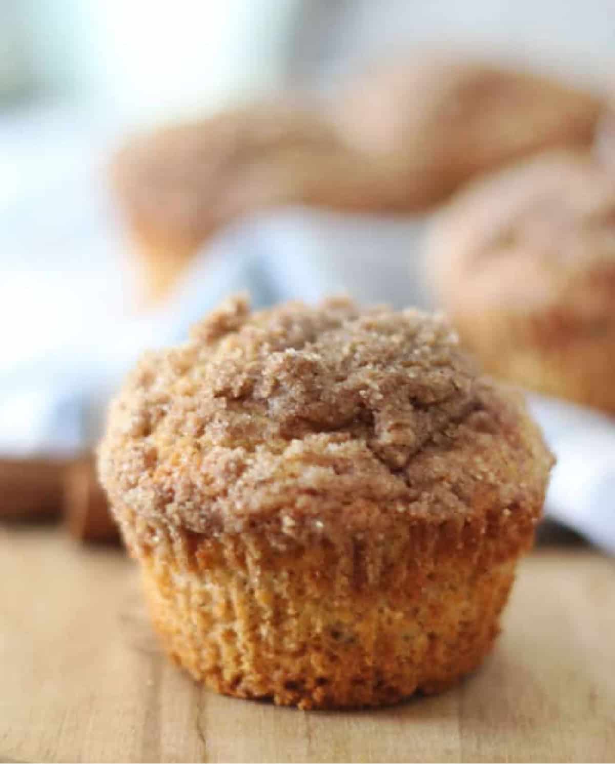 Apple cider muffin on wood table with muffins in the background.