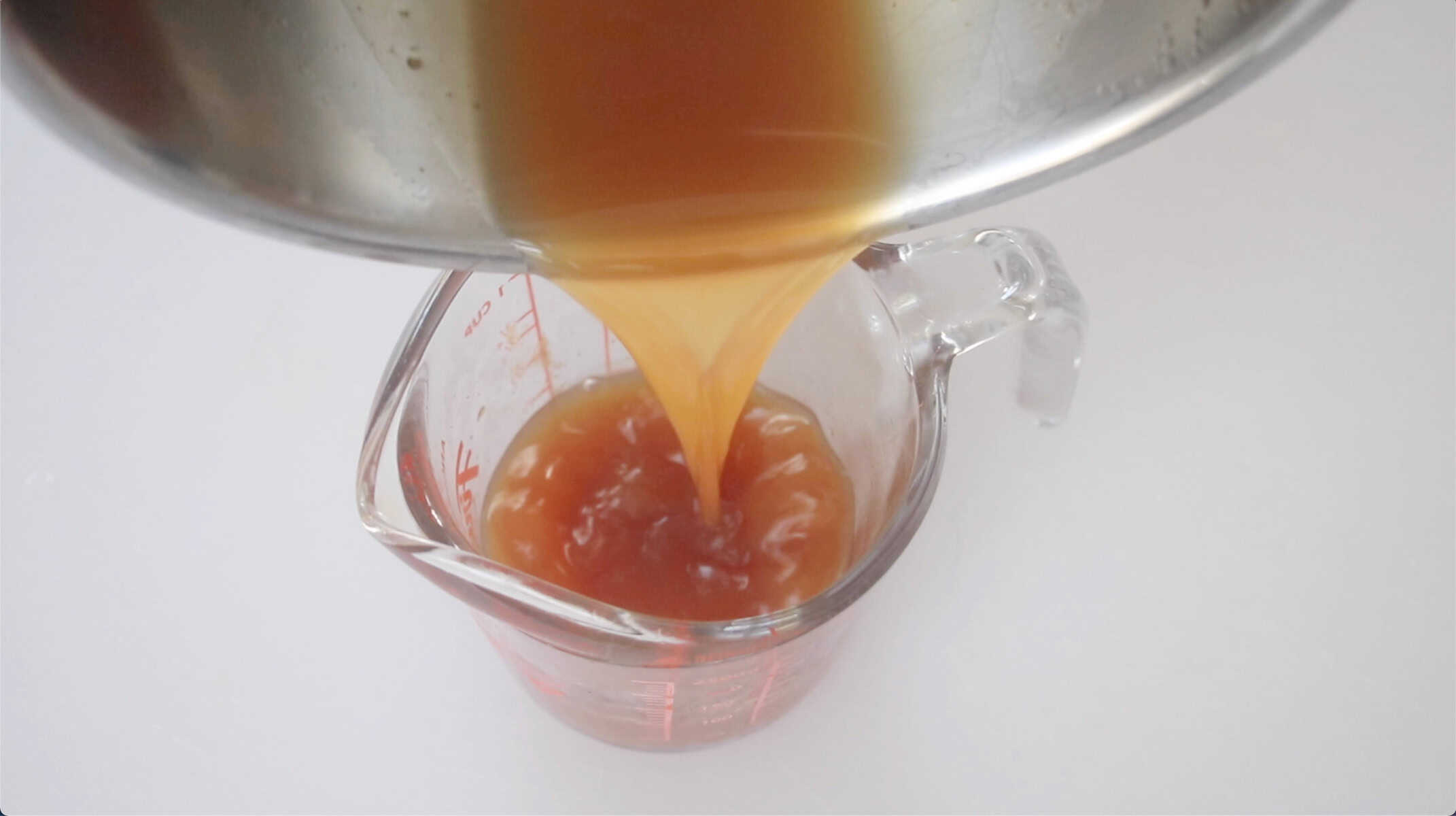 Apple cider being poured into a glass measuring cup.