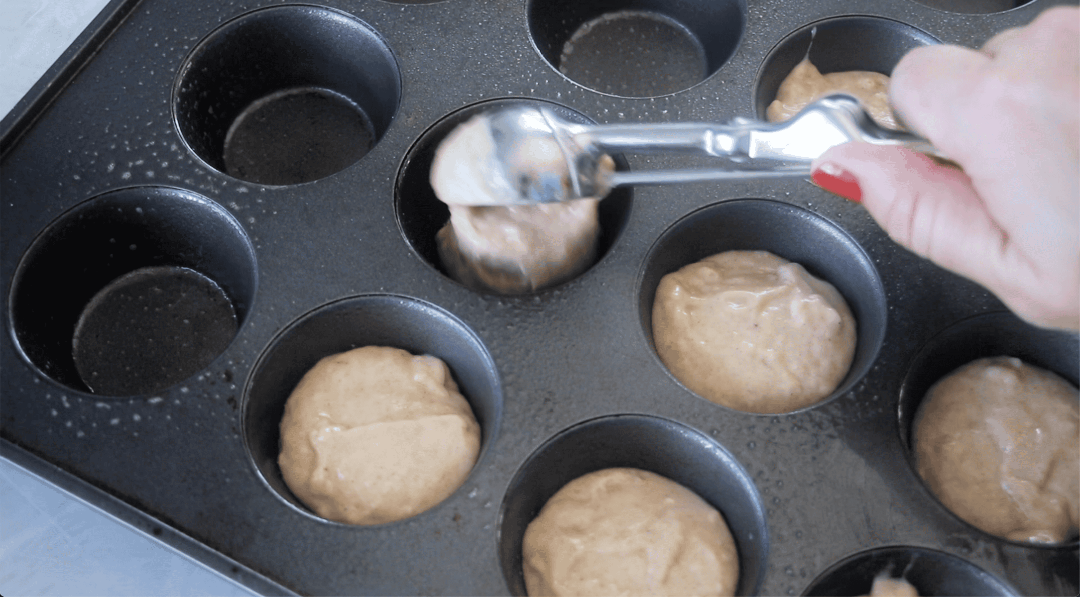 Metal muffin pan with unbaked muffin batter scooped into the cavities.