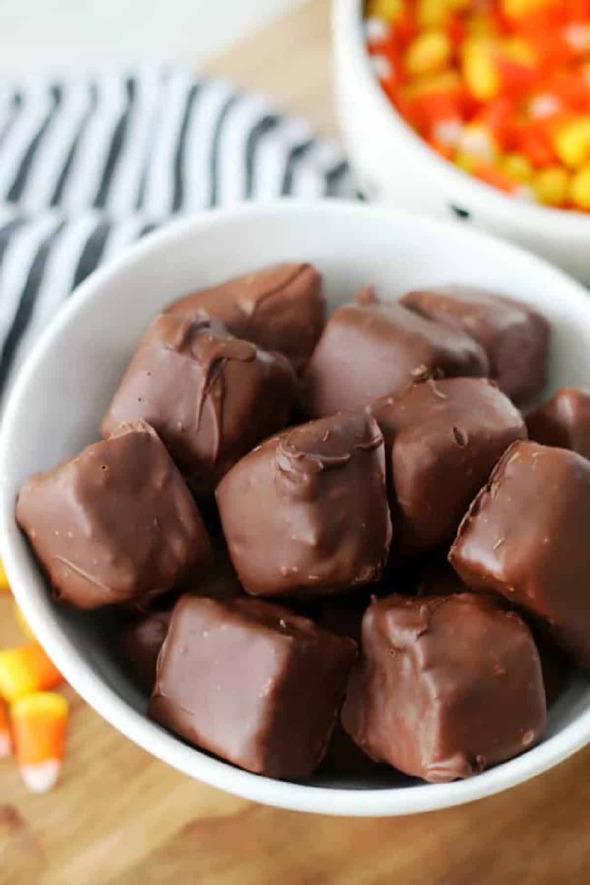 Homemade butterfingers in a white bowl next to a bowl of candy corn.