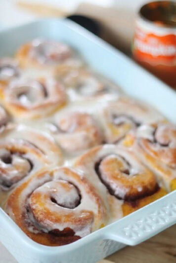 Baking dish with pumpkin cinnamon rolls frosted with buttercream.