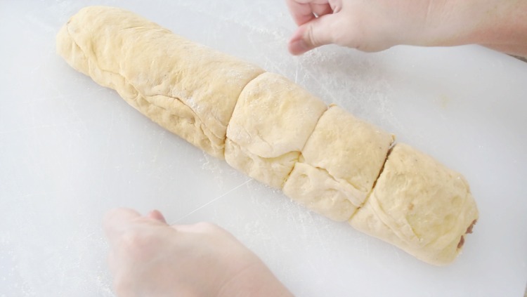 rolled up cinnamon roll dough being sliced into sections