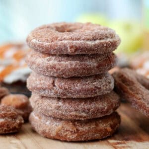 Stack of apple cider donuts covered in cinnamon and sugar on wooden cutting board.