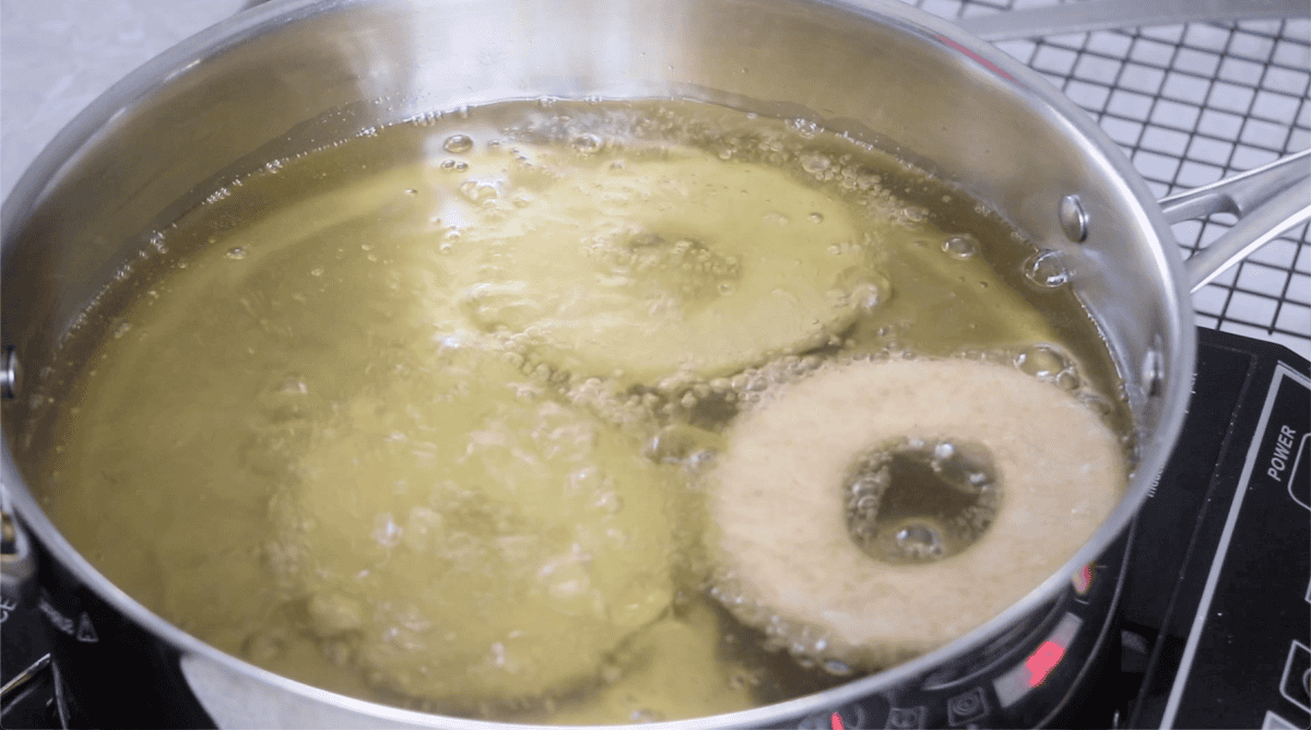 3 donuts in pan with bubbling oil.
