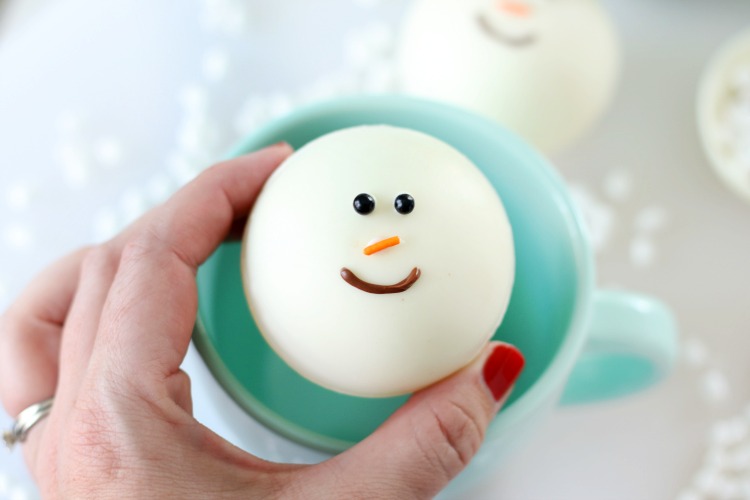 hand holding snowman hot chocolate bombs over mug