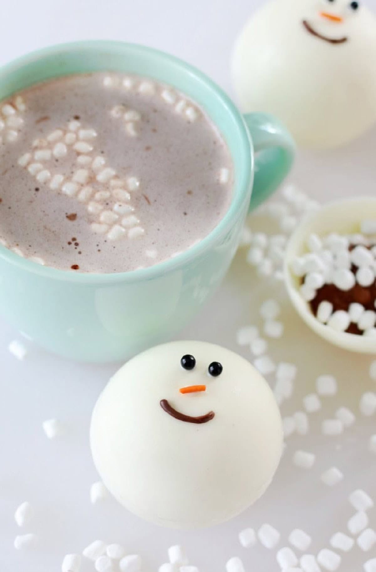Snowman cocoa bomb next to mint green mug.