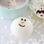 Snowman cocoa bomb next to green mug.