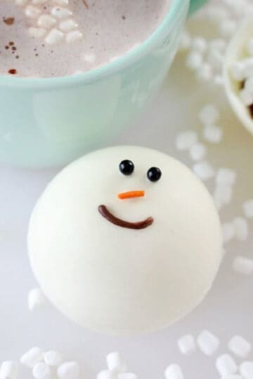 Snowman cocoa bomb next to green mug.