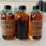 Three bottles of vanilla extract with green ribbon tied around the lid.