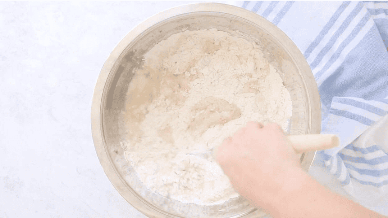 Metal mixing bowl of bread dough and dough whisk.