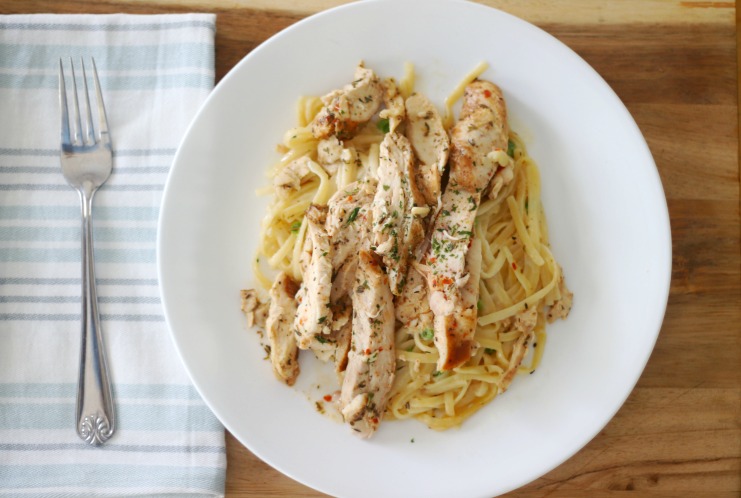 white plate with chicken fettuccini next to cloth napkin