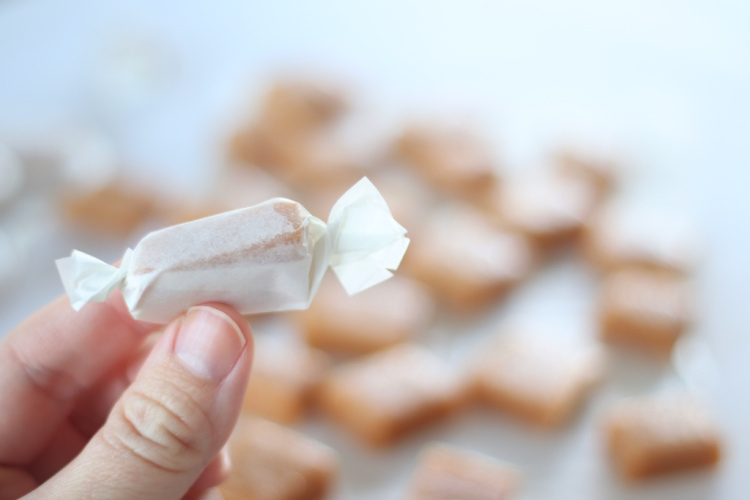 hand holding caramel candy wrapped in parchment paper