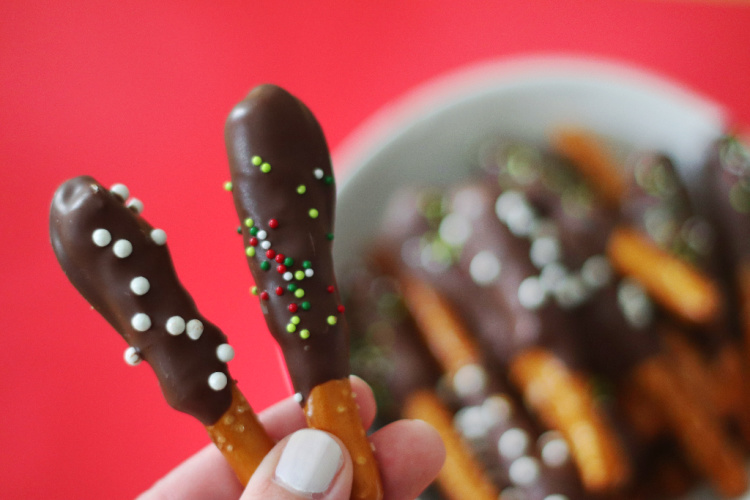 hand holding two pretzel rods dipped in chocolate and peanut butter