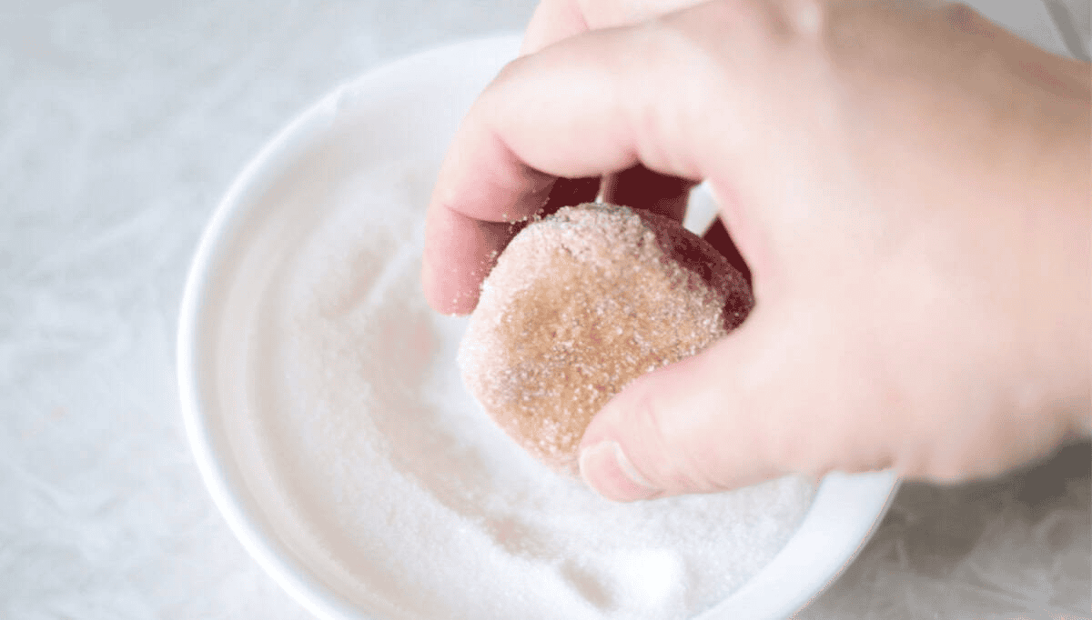 Hand rolling cookie dough ball in sugar.