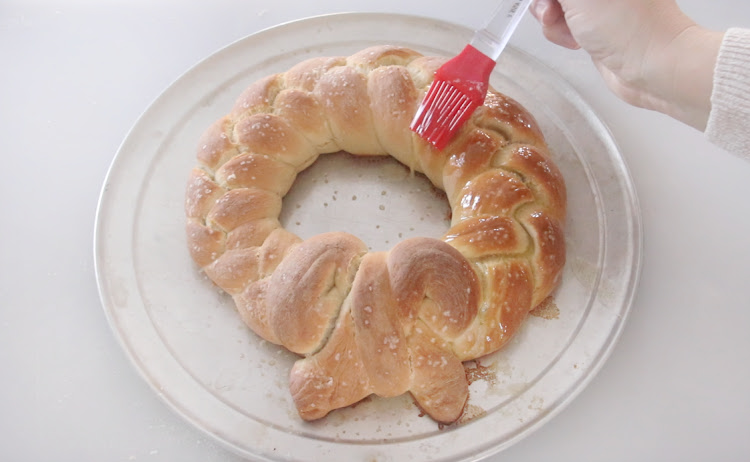 hands brushing butter on pretzel wreath with pastry brush