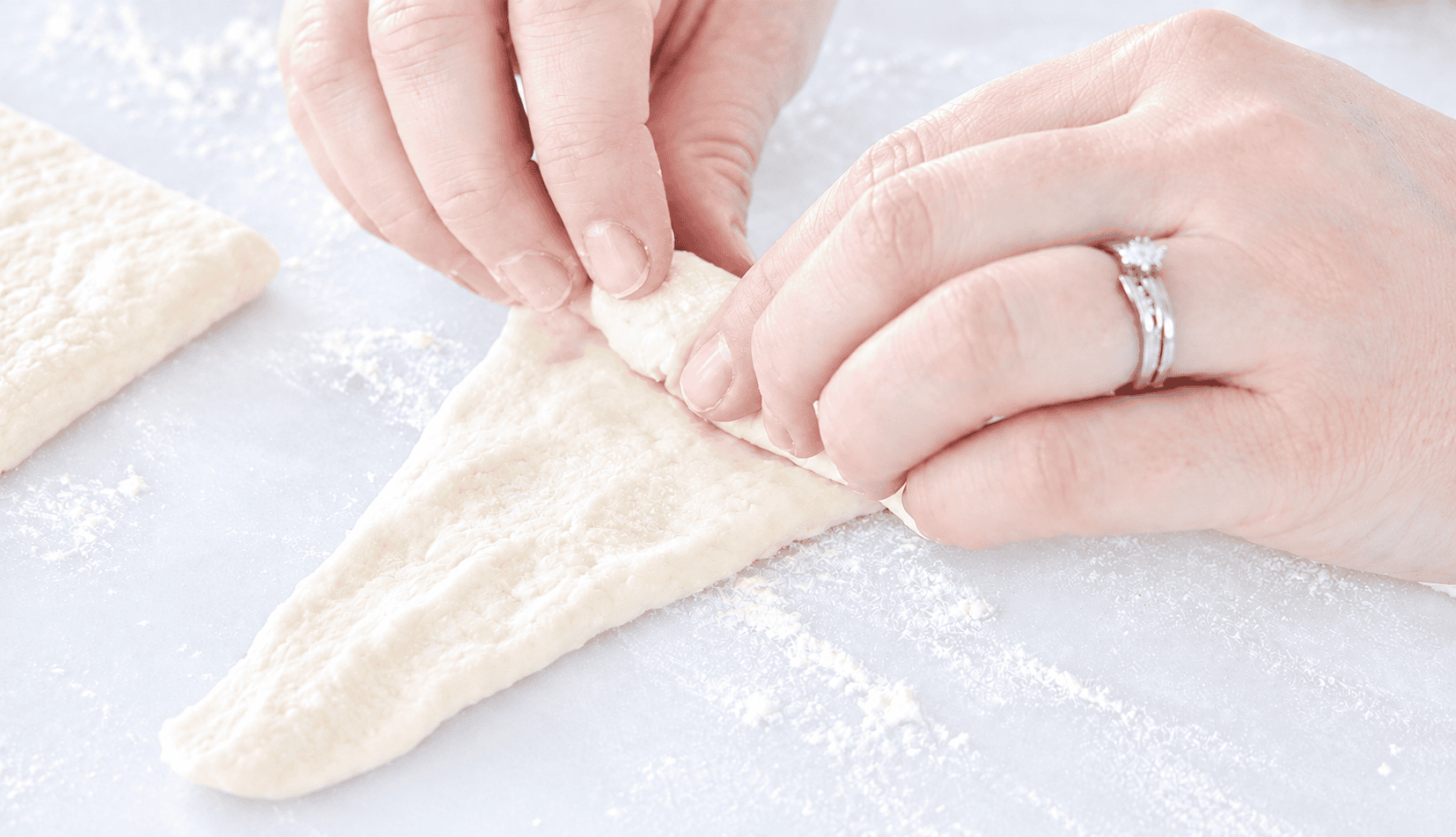 Hands rolling triangles of dough into croissant shapes.