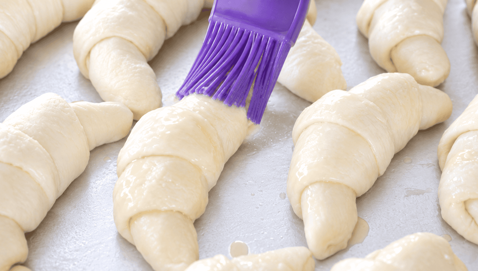 Pastry brush brushing egg wash on the croissants.