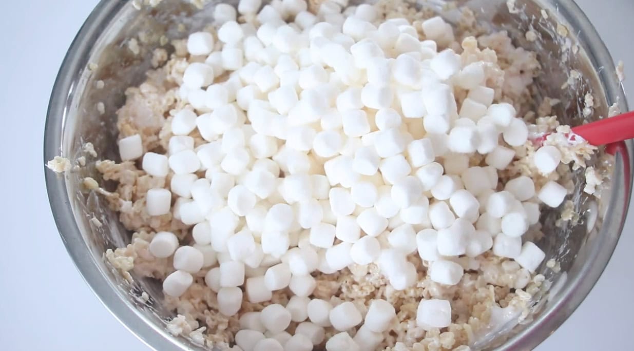 Large metal mixing bowl with extra marshmallows poured over rice krispies treats mixture.