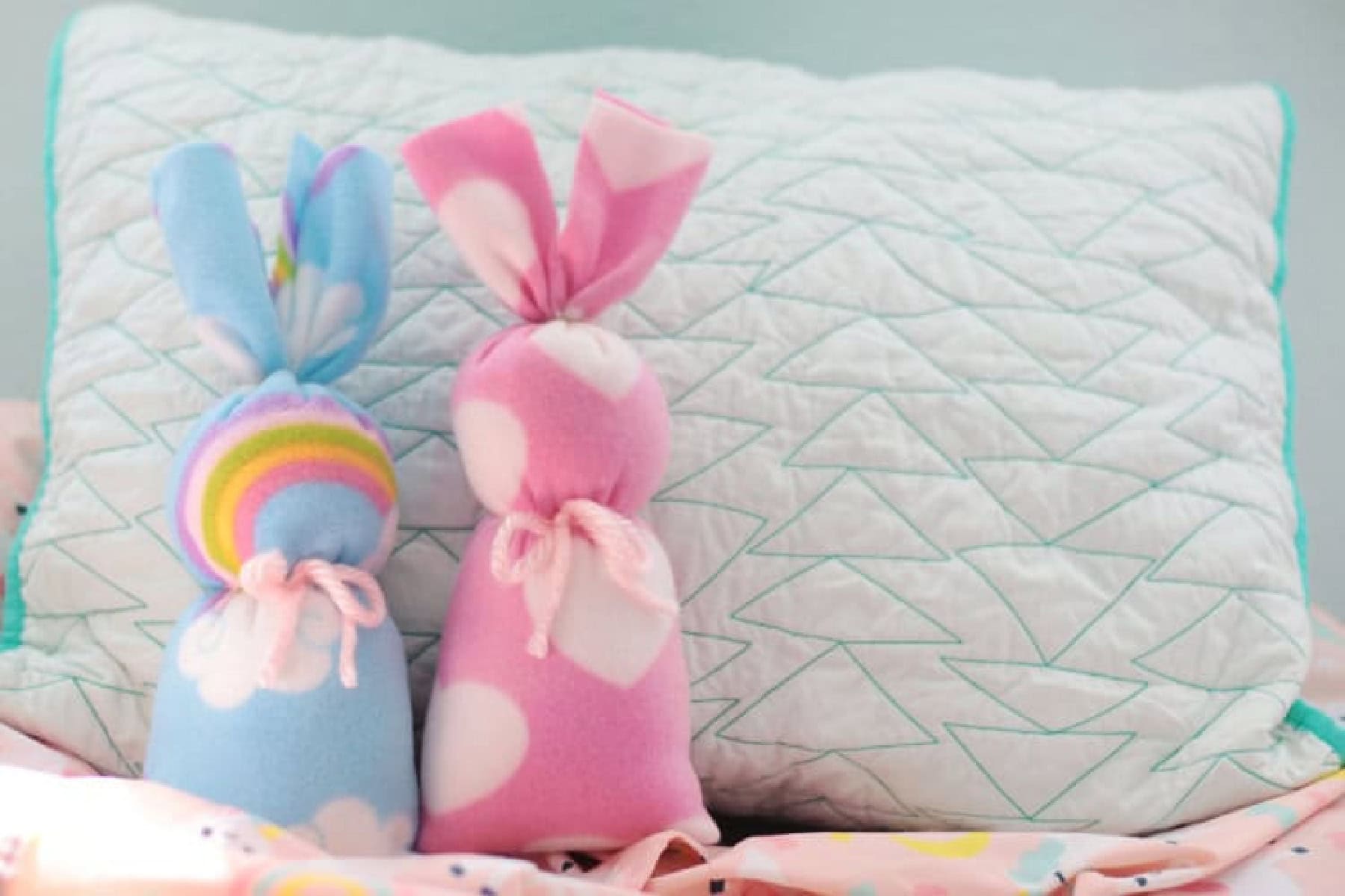 Two fleece bunnies in front of a pillow.