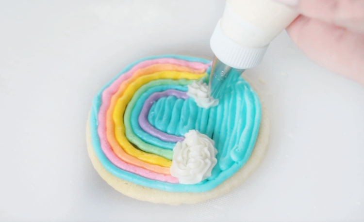 round rainbow cookie with clouds being piped onto it