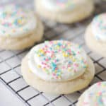 Frosted sugar cookies with sprinkles on wire rack.