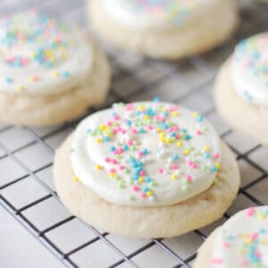 Frosted sugar cookies with sprinkles on wire rack.
