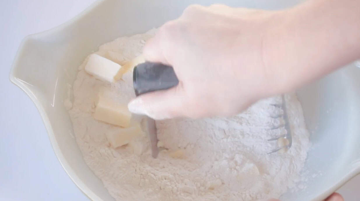 Pastry cutter cutting cold butter into the flour in mixing bowl.