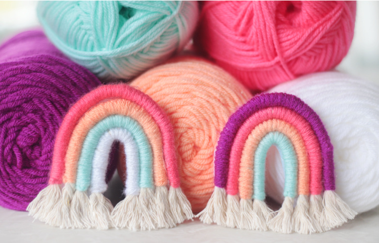 two yarn wrapped rainbow crafts next to pile of yarn skeins