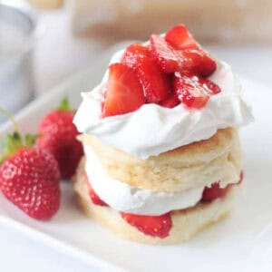 Biscuits, cream and strawberries stacked on white plate.